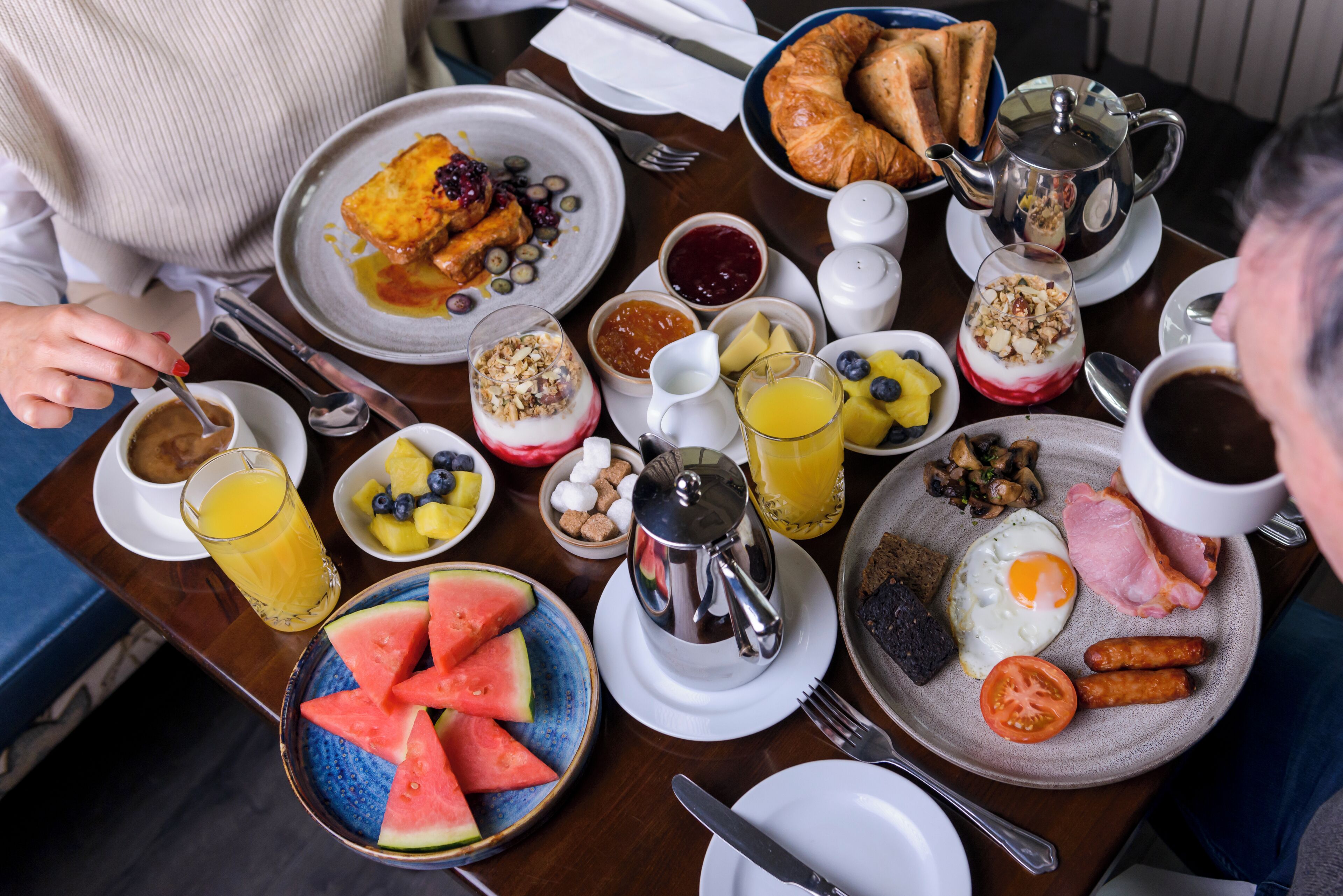 Ein Frühstückstisch mit verschiedenen Speisen, darunter Eier, Würstchen, Toast und Obst.