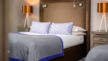 A neatly made bed with patterned pillows, a brown upholstered headboard, and two bedside lamps.