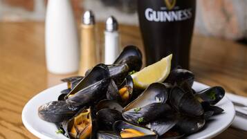 Une assiette de moules accompagnée de quartiers de citron, un vase blanc rempli de fleurs et un grand verre de bière Guinness sur une table en bois.