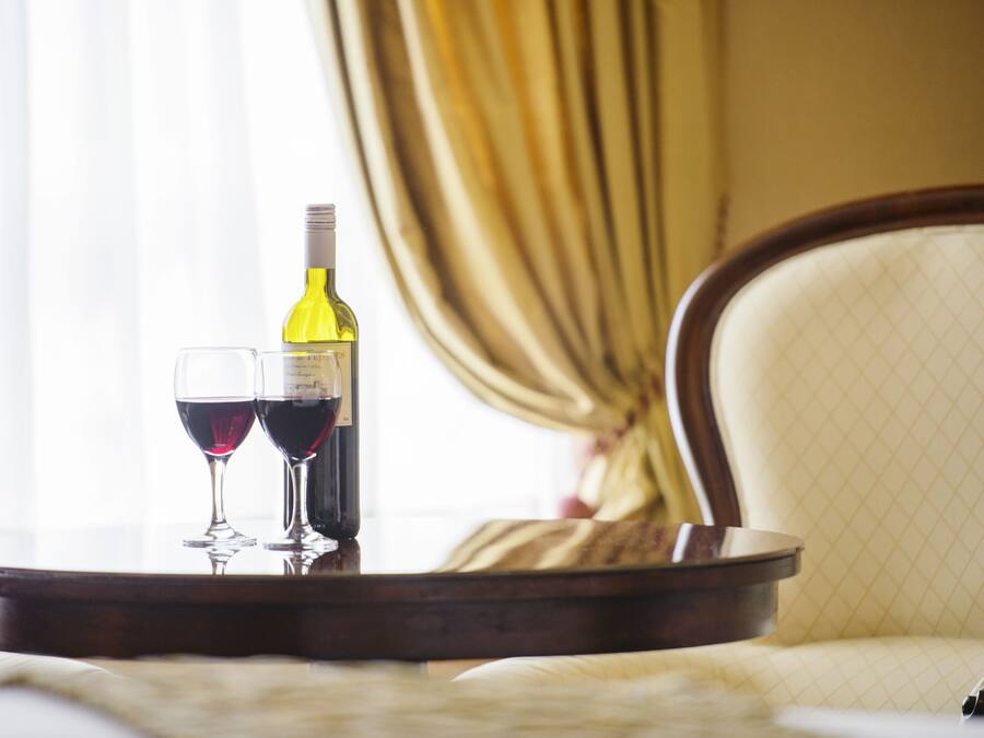Een tafel met een fles wijn en twee glazen, in een kamer met een stoel en gordijnen.