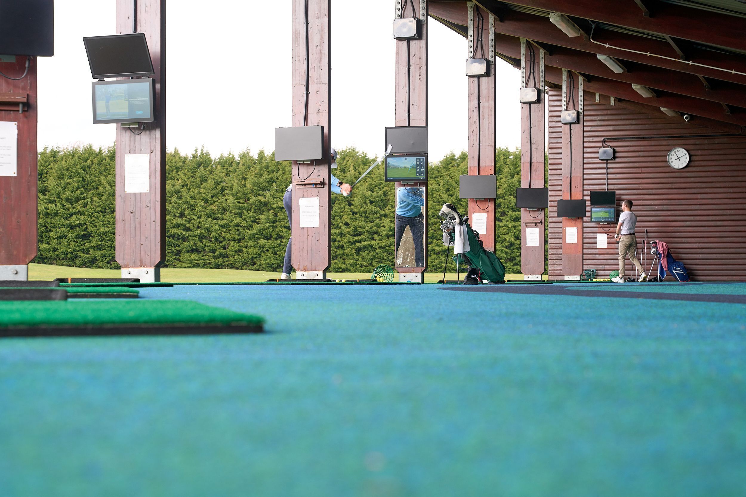 Un campo de prácticas de golf con múltiples pantallas y objetivos, un reloj y un campo verde.