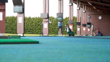 Un campo de prácticas de golf con múltiples pantallas y objetivos, un reloj y un campo verde.