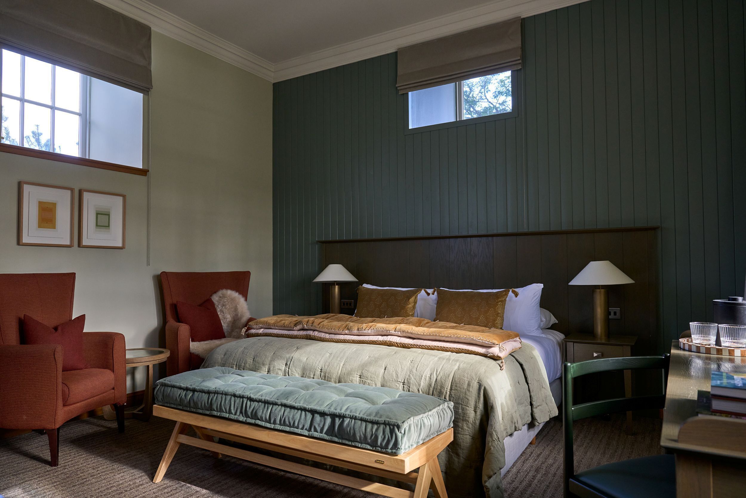 Un dormitorio con cama, dos sillas, un banco, una mesita de noche y una lámpara.