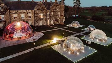 Edificio histórico de piedra con un patio que cuenta con estructuras de cúpulas transparentes y asientos.