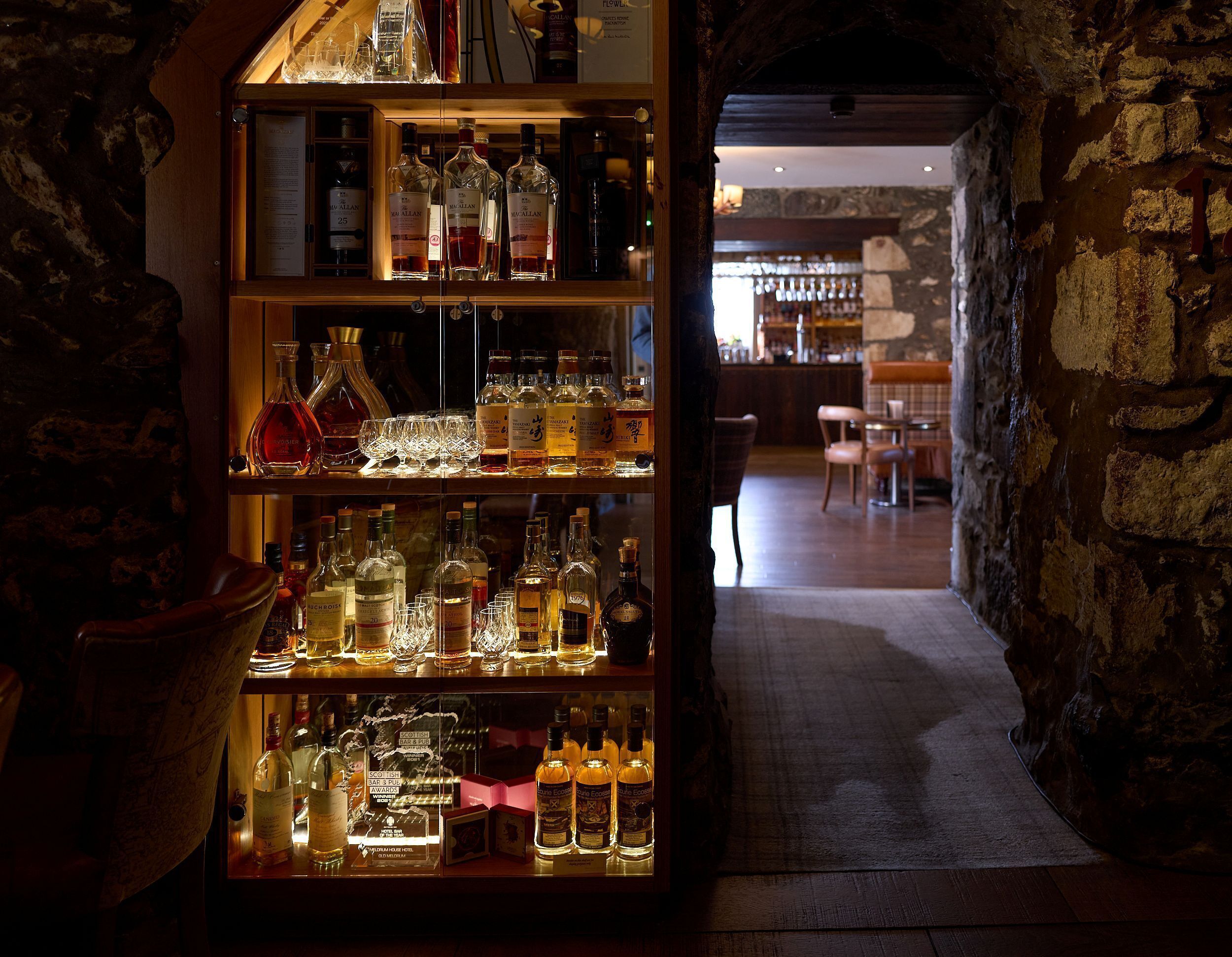 Een bar met flessen drank en glazen op de planken.