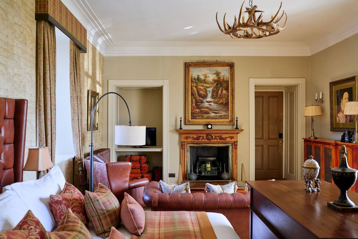 A room with a bed, a sofa, a fireplace, a painting, and a chandelier.