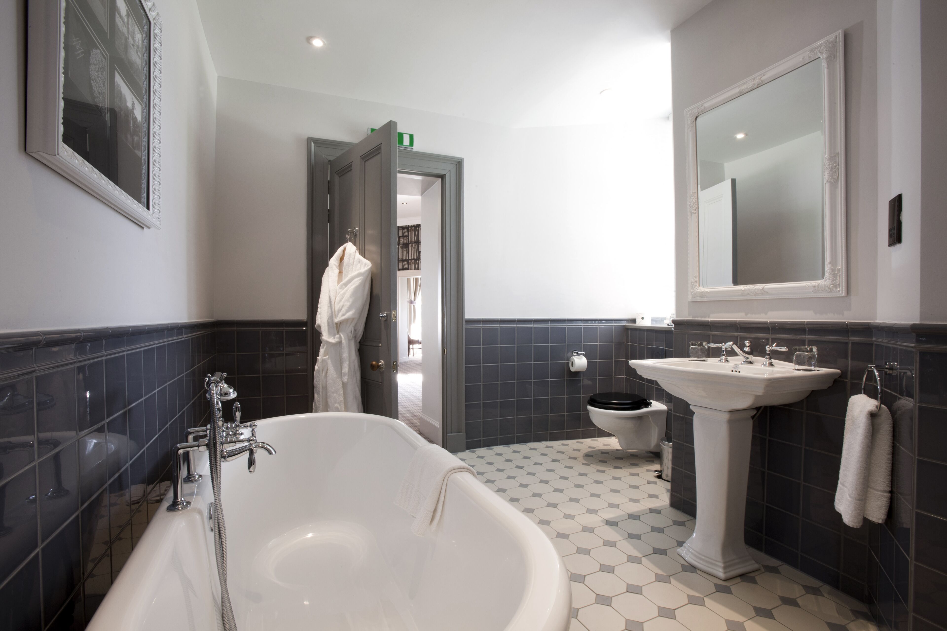 A modern bathroom with a freestanding bathtub, a pedestal sink, and a large mirror.