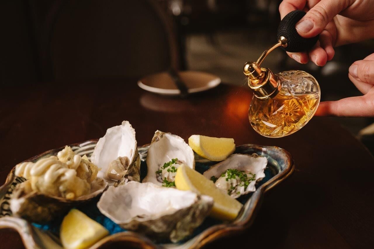 Una mano sosteniendo una botella de licor, un plato de ostras y gajos de limón.