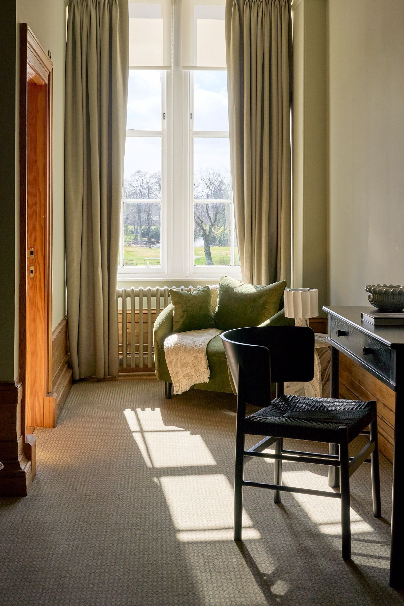 A room with a bed, a chair, a table, and a window with curtains.