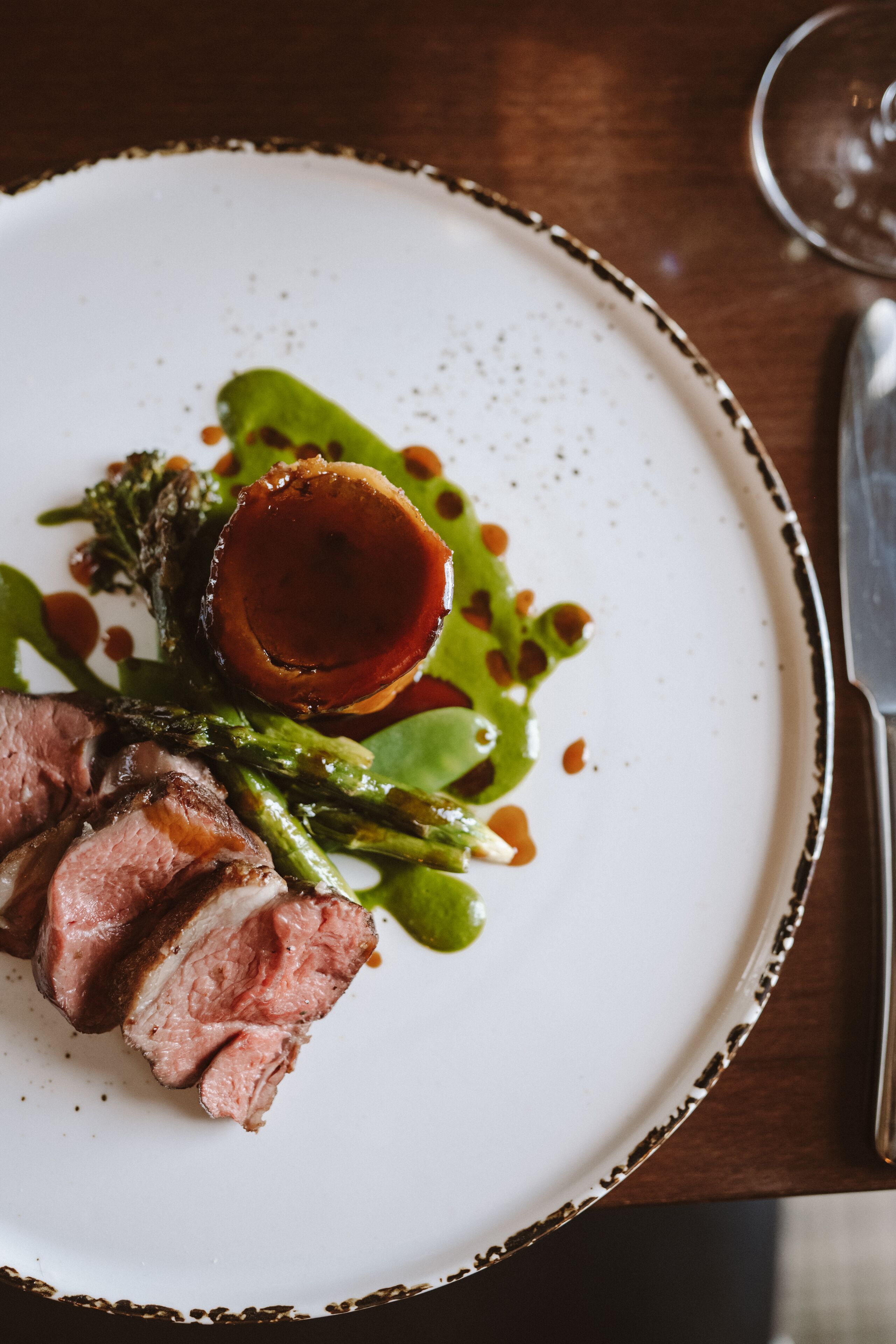Um prato com carne fatiada, aspargos e um detalhe decorativo em um prato branco.