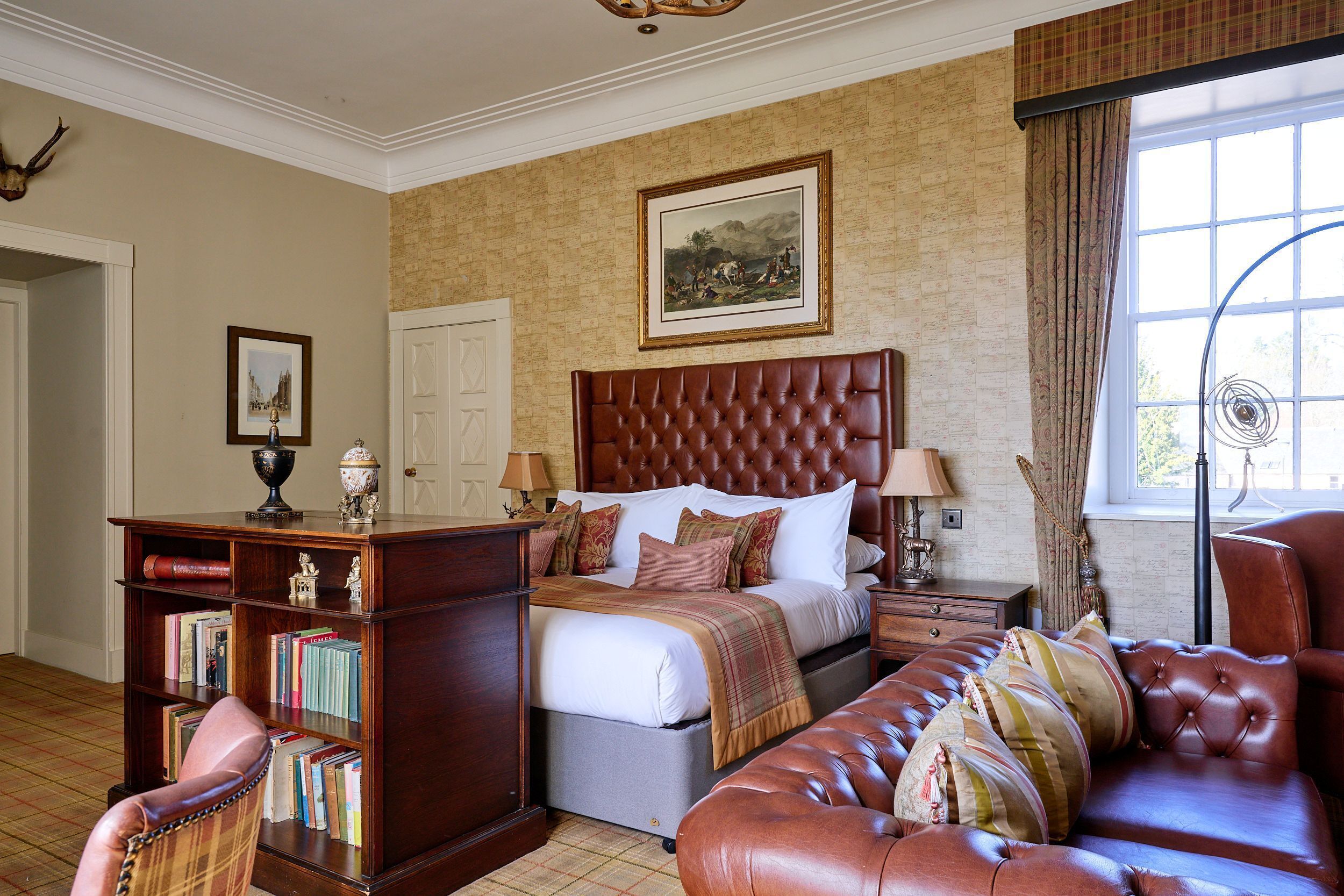 A bedroom with a large bed, a wooden nightstand, a leather armchair, a bookshelf, and a window with curtains.