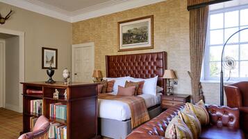 A bedroom with a large bed, a wooden nightstand, a leather armchair, a bookshelf, and a window with curtains.