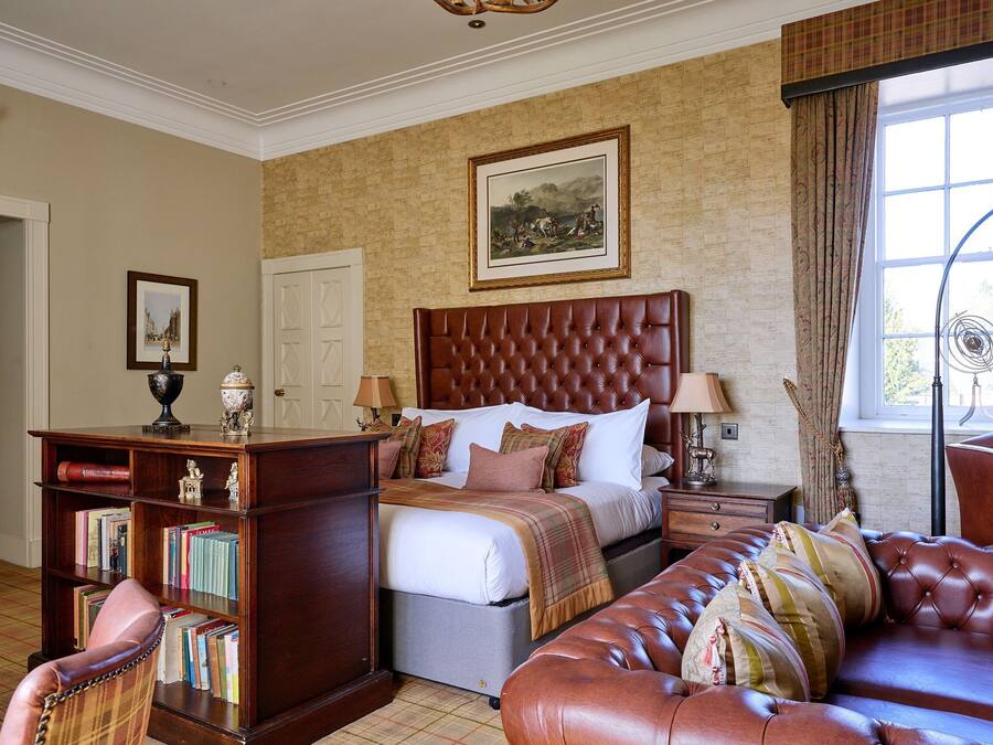 A bedroom with a large bed, a wooden nightstand, a leather armchair, a bookshelf, and a window with curtains.