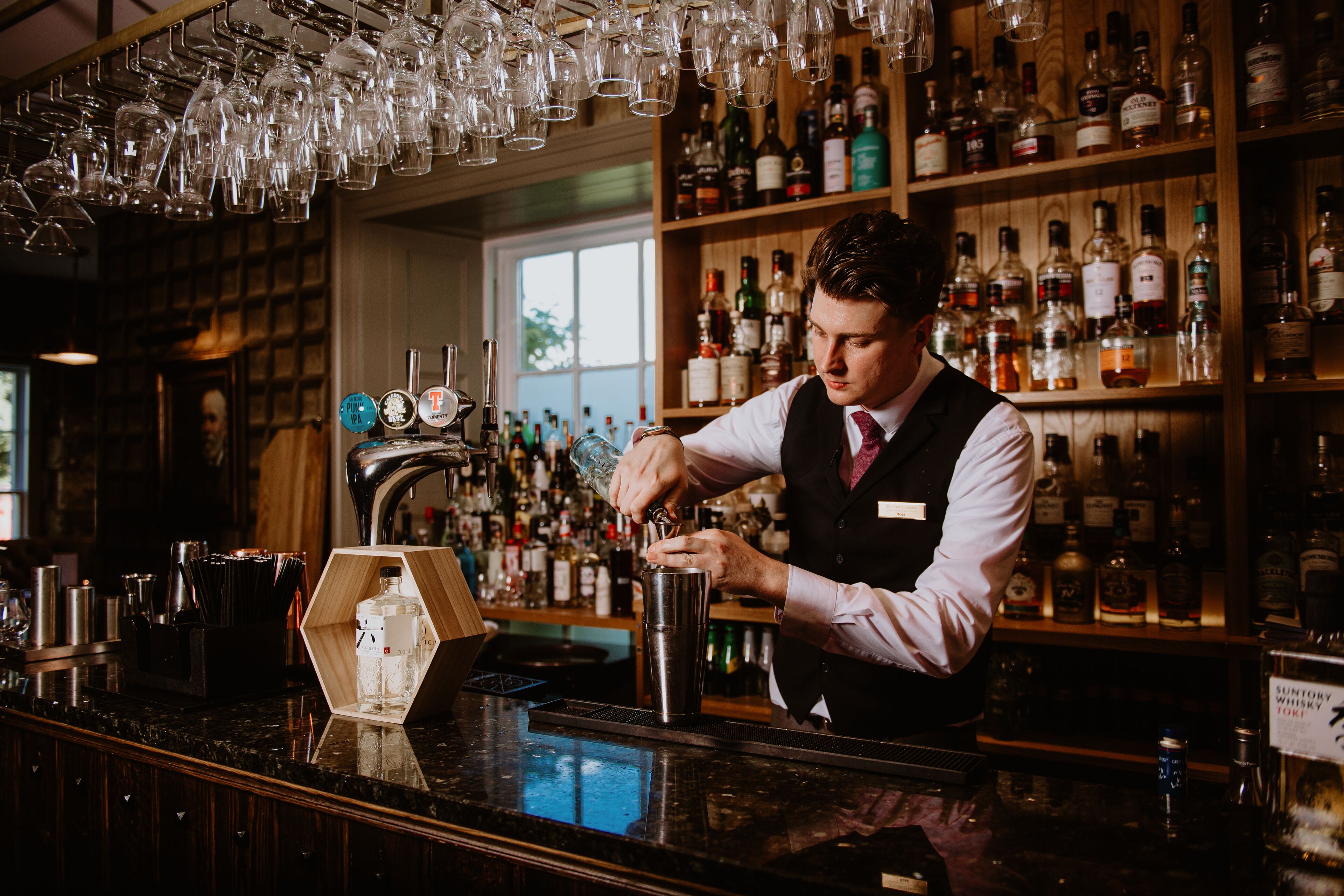 Ein Barkeeper hinter einer Bar, im Hintergrund eine Auswahl an Spirituosenflaschen.