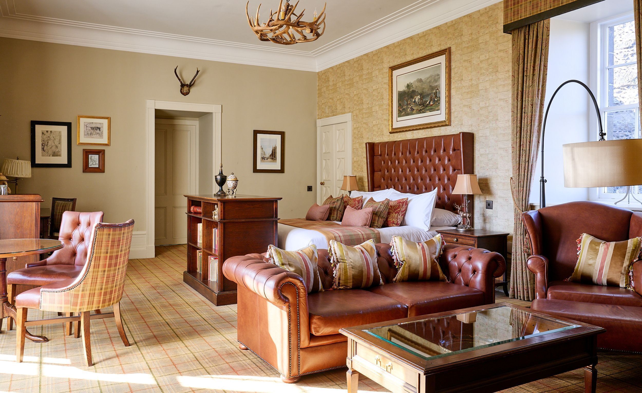 Habitación de hotel con cama, muebles de cuero, una araña y obras de arte en las paredes.