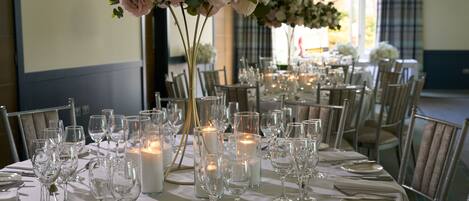 A banquet hall with tables set for dining, candles, and floral centerpieces.