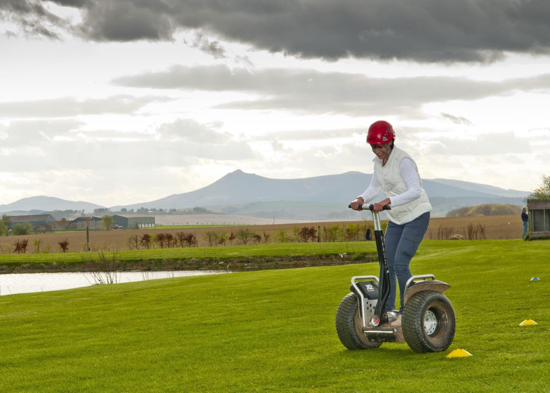 Henkilö ajaa Segway-laitteella ruohikkoisella pellolla, taustalla näkyy vuori.