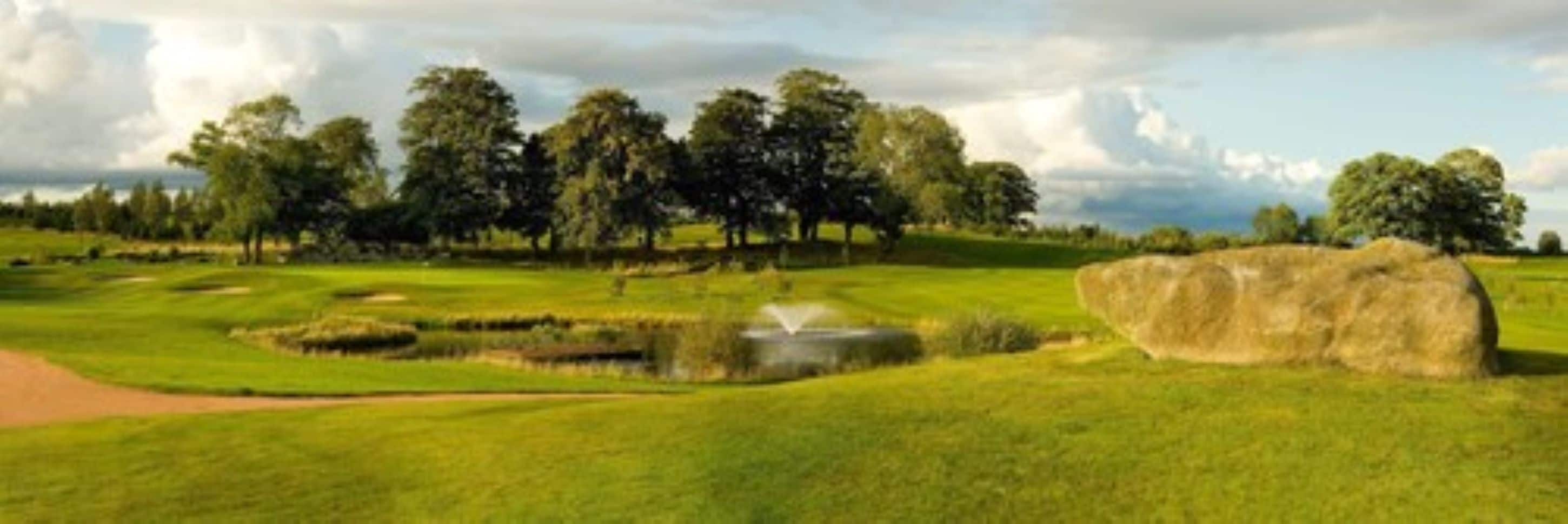 A golf course with a pond, trees, and a large rock.