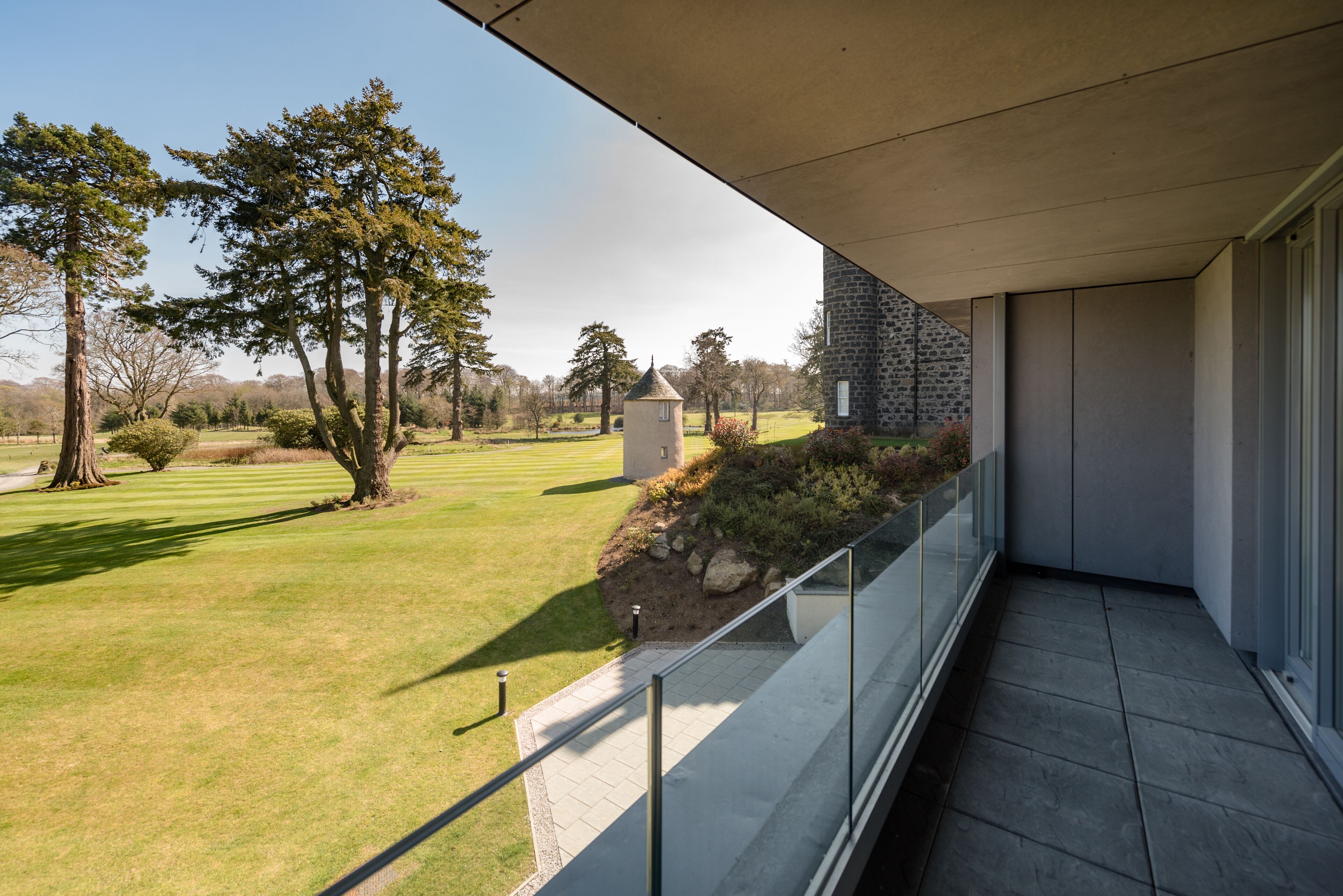 A balcony with a view of a well-manicured lawn and a stone building.