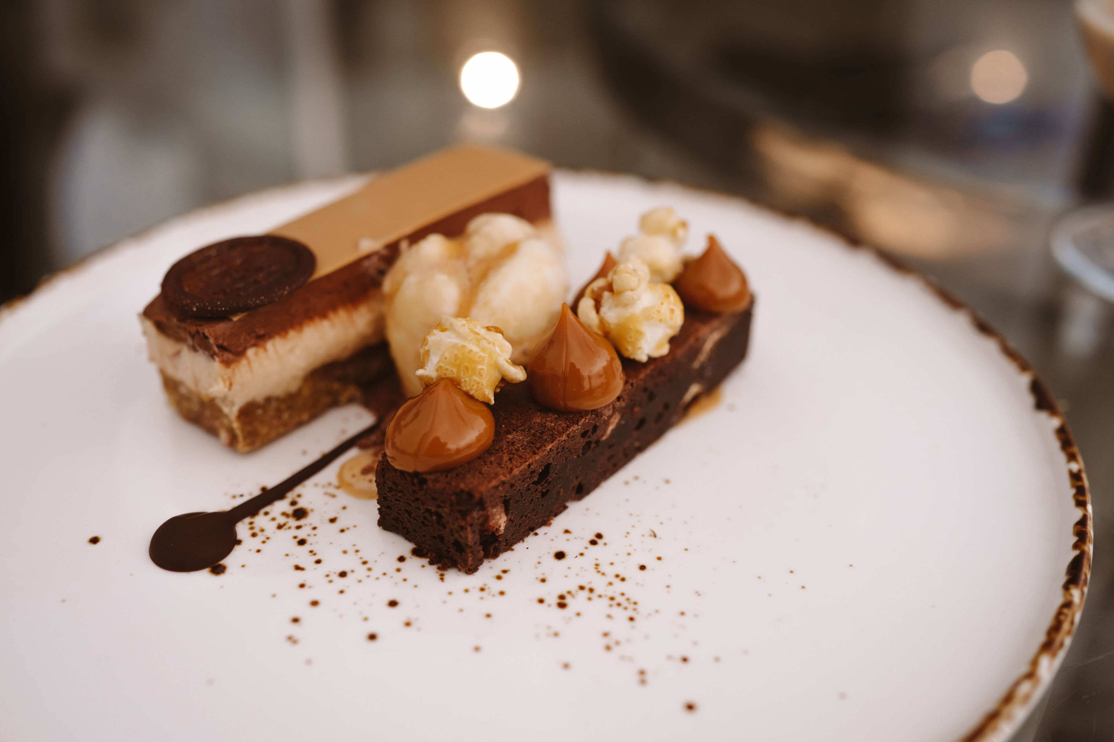 Un dessert servi dans une assiette, composé d’un morceau de chocolat, d’une boule de glace et de caramel.