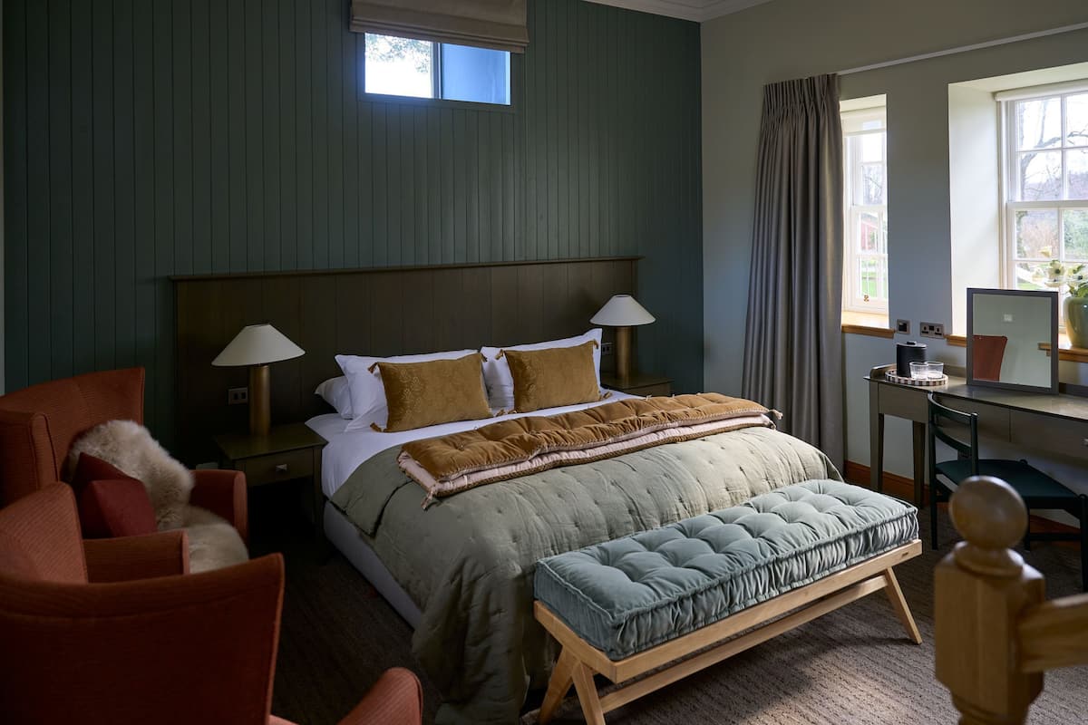 A bedroom with a bed, bedside lamps, a desk, a chair, and a window with curtains.
