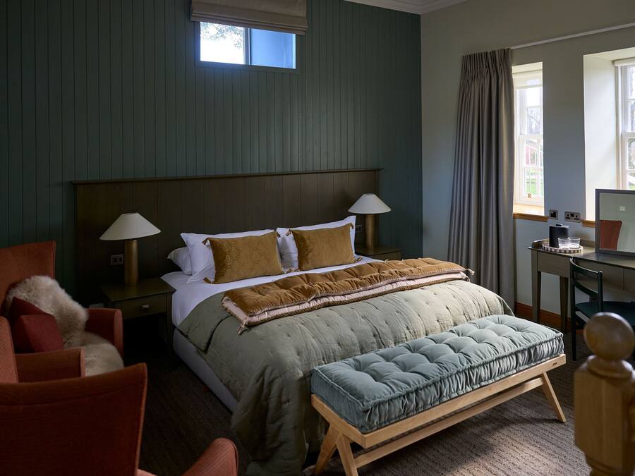 Ein Schlafzimmer mit Bett, Nachttischlampen, Schreibtisch, Stuhl und einem Fenster mit Vorhängen.
