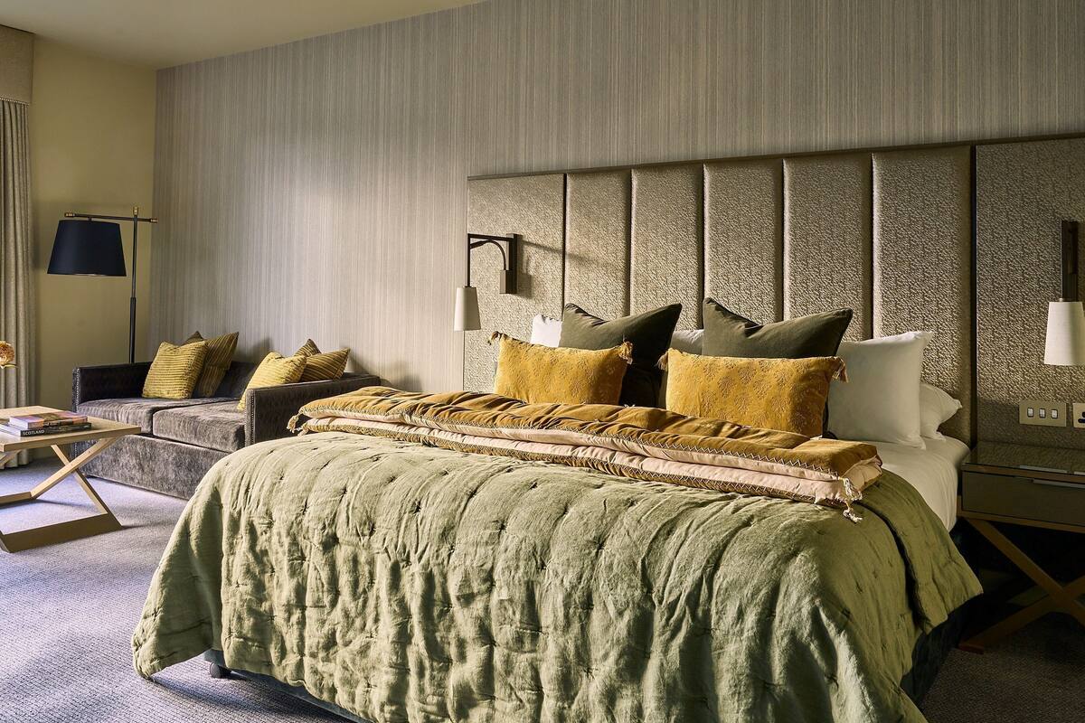 A bedroom with a large bed, a bedside table, a lamp, and a sofa.
