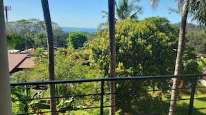 A balcony with a view of a lush garden and a distant body of water.
