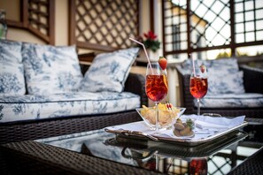 A tray with two drinks, a bowl of snacks, and a glass of olives on a table in a room with patterned cushions and lattice windows. - Romantik Hotel Villa Margherita (Mira)
