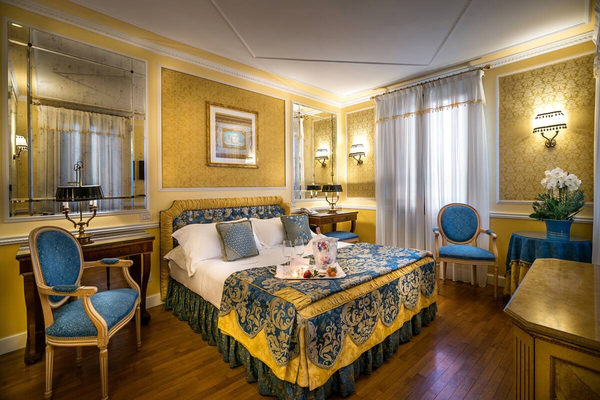 Un dormitorio espacioso con una cama grande, un rincón de estar con una mesa y sillas, y un espejo.