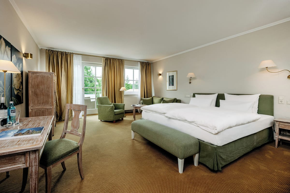 Une chambre d’hôtel avec un grand lit, un bureau avec une chaise, une petite table et une fenêtre avec des rideaux.