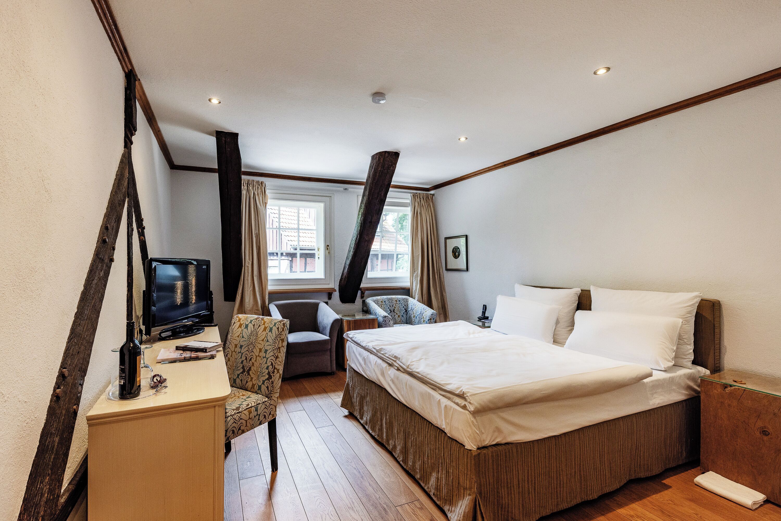 A hotel room with a bed, a desk with a television, a chair, and a window with curtains.
