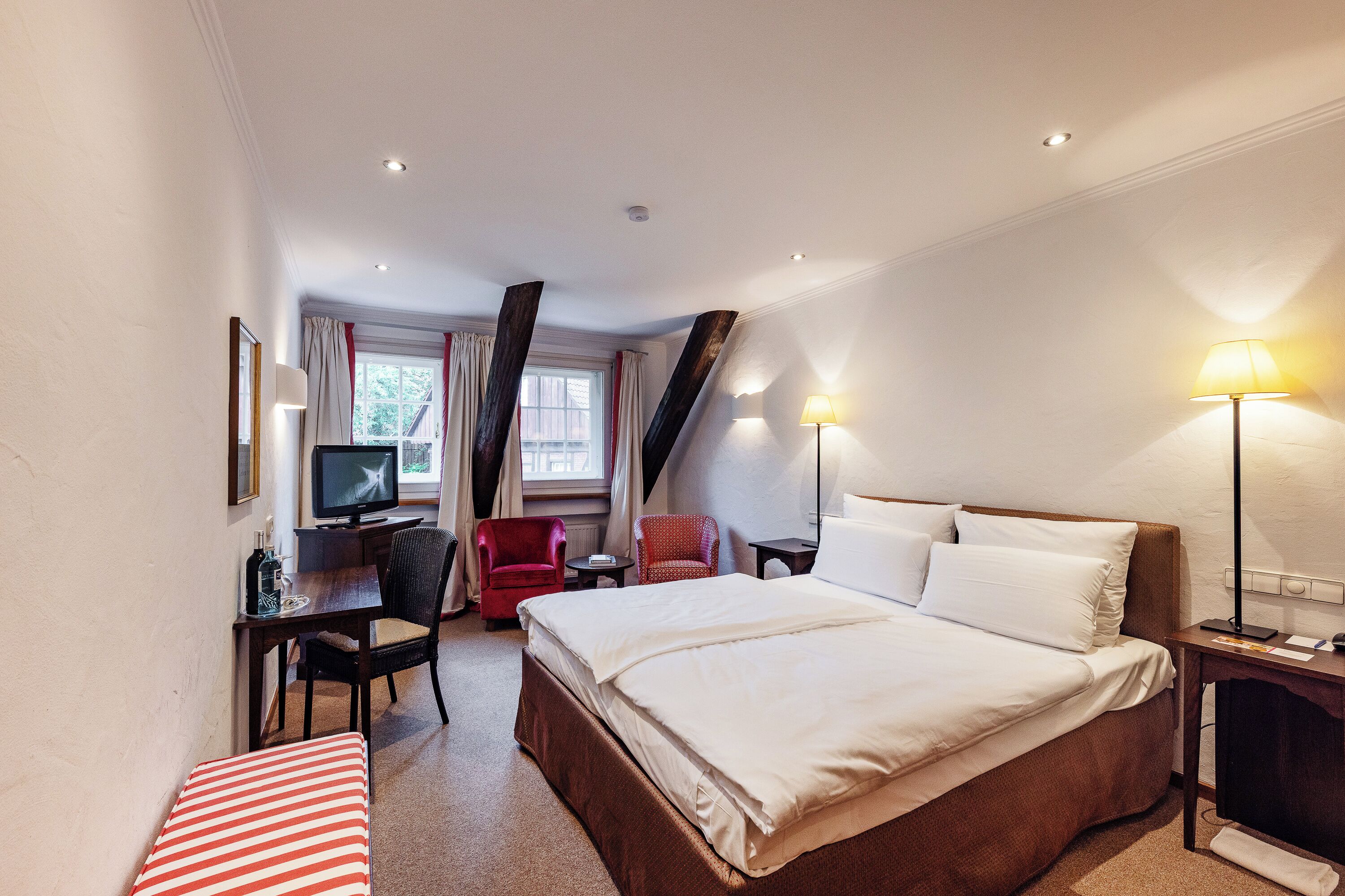 A hotel room with a bed, a desk with a computer, a chair, a television, and a lamp.