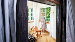 Una habitación con piso de madera, una mesa con una revista y una ventana con cortinas blancas.