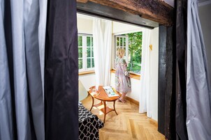 Una habitación con piso de madera, una mesa con una revista y una ventana con cortinas blancas.