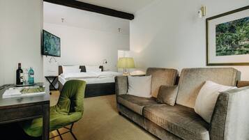 A hotel room with a bed, a green chair, a sofa, a desk with a lamp, and a TV on the wall.