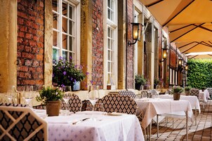 Un espacio de comedor al aire libre con paredes de ladrillo, marcos de ventana blancos y mesas listas para cenar.