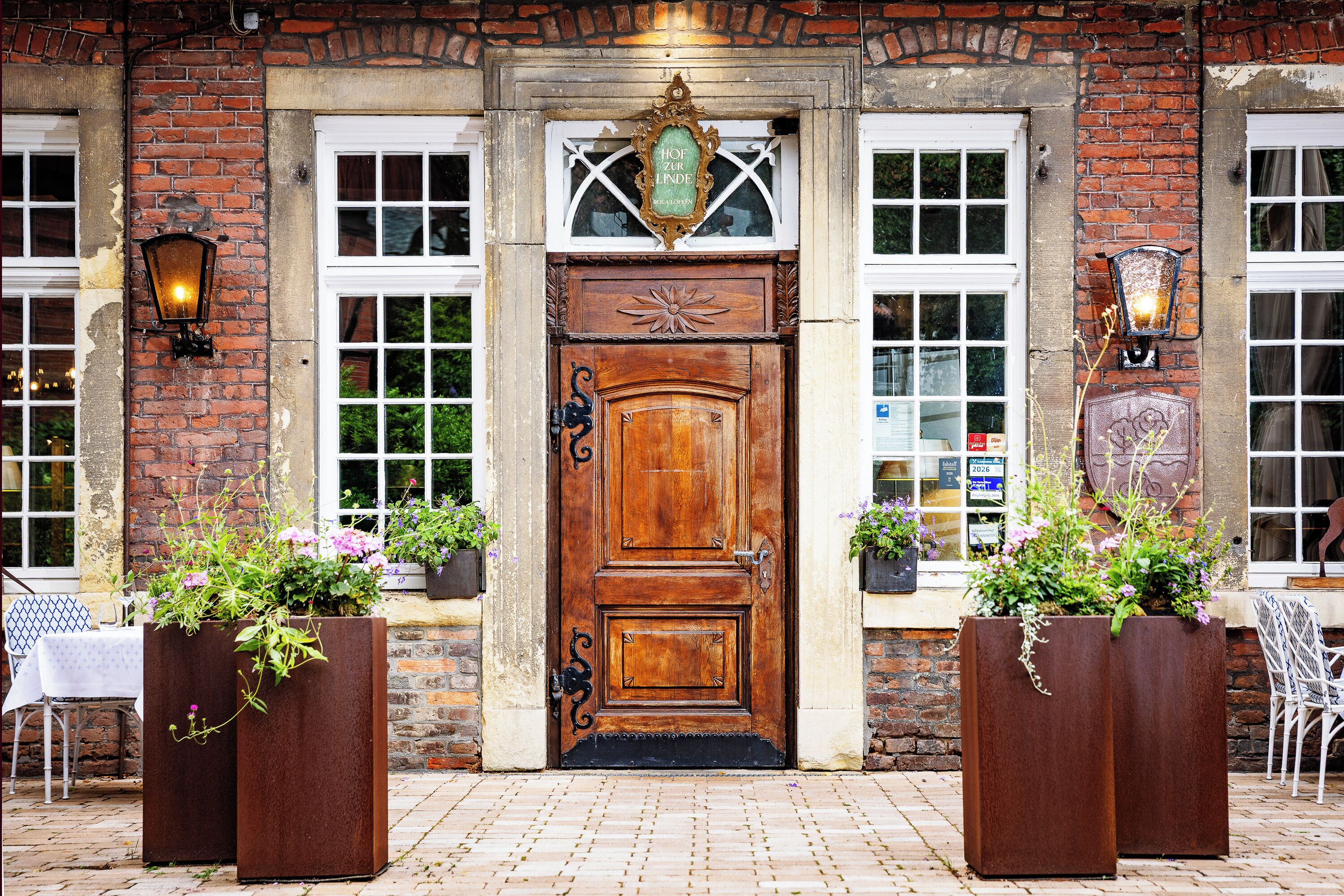 A brick building with a wooden door, two windows with white frames, and decorative wall sconces.