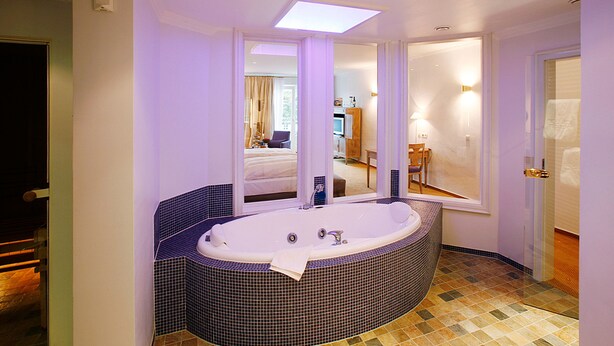 Un baño con una bañera grande, un espejo y vistas a un dormitorio.