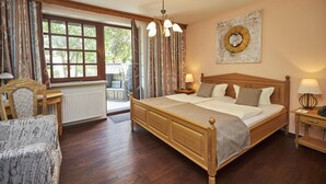 A bedroom with a wooden bed, a nightstand with a lamp, a chair, a window with curtains, and a wall with a decorative plate.