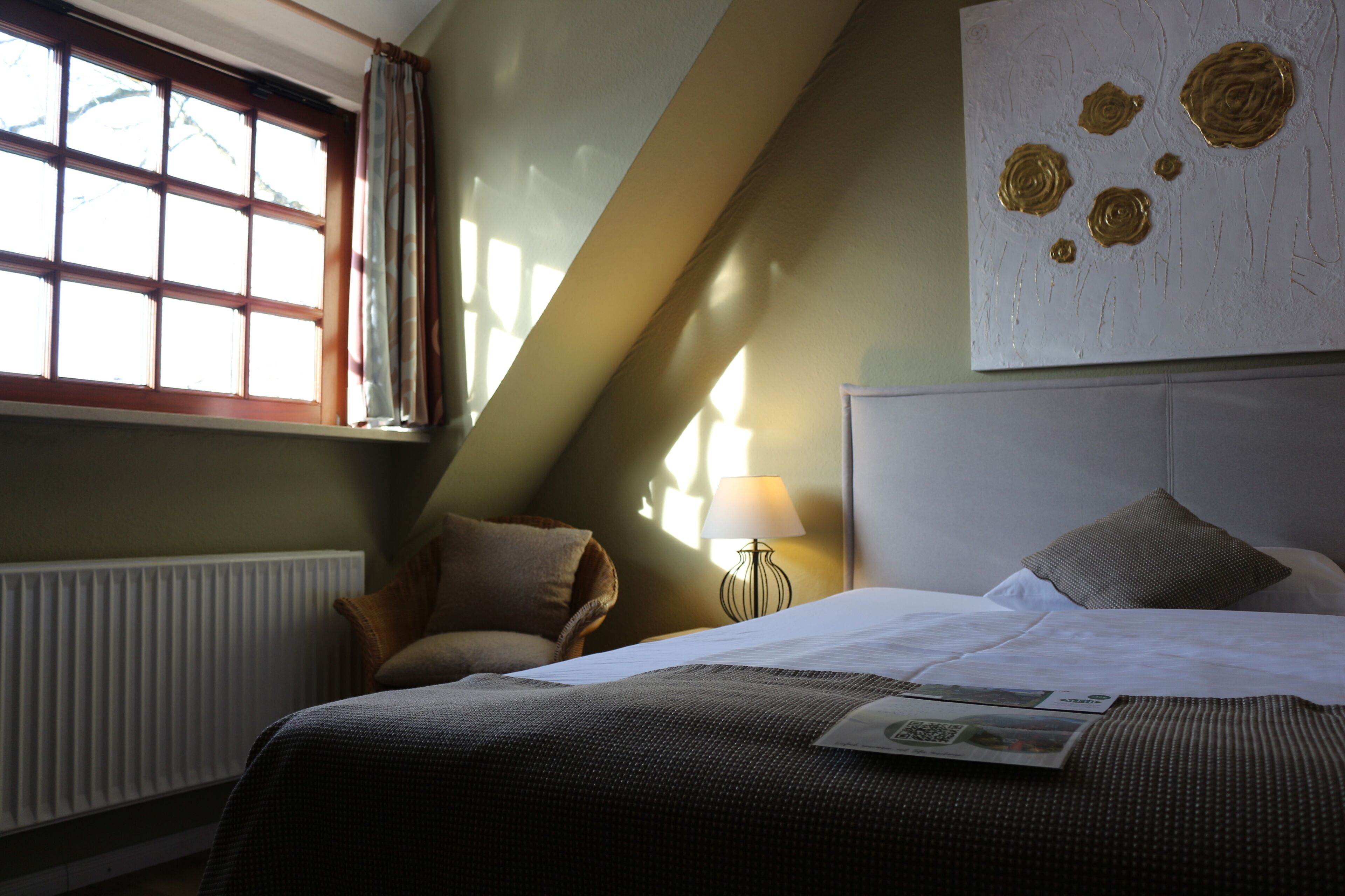 A hotel room with a bed, a window with curtains, a lamp, and a wall art piece.