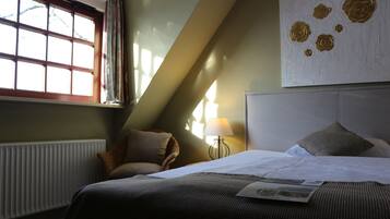 A hotel room with a bed, a window with curtains, a lamp, and a wall art piece.