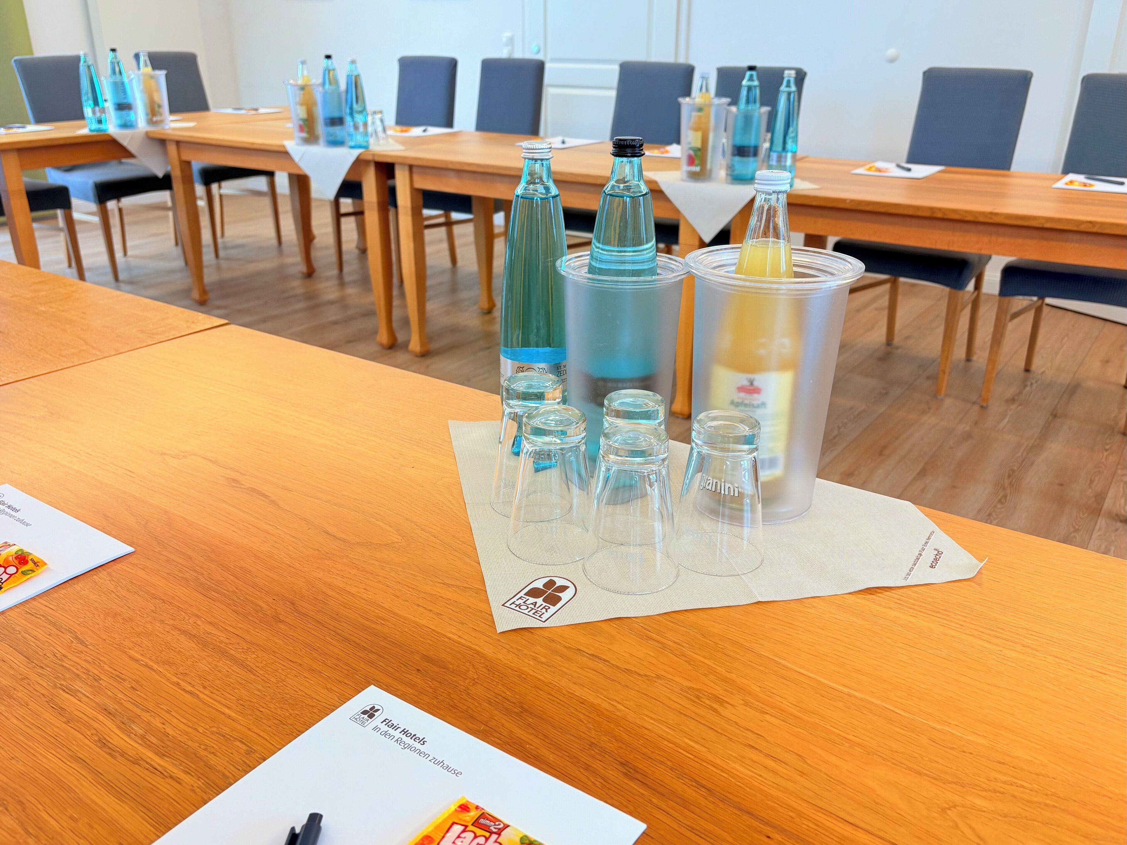 Un salón de conferencias con mesas de madera, botellas de vidrio transparente y una pizarra.
