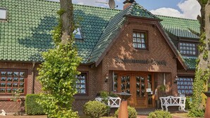 A traditional brick building with a green tiled roof, a wooden front door, and a sign that reads "Restaurant".