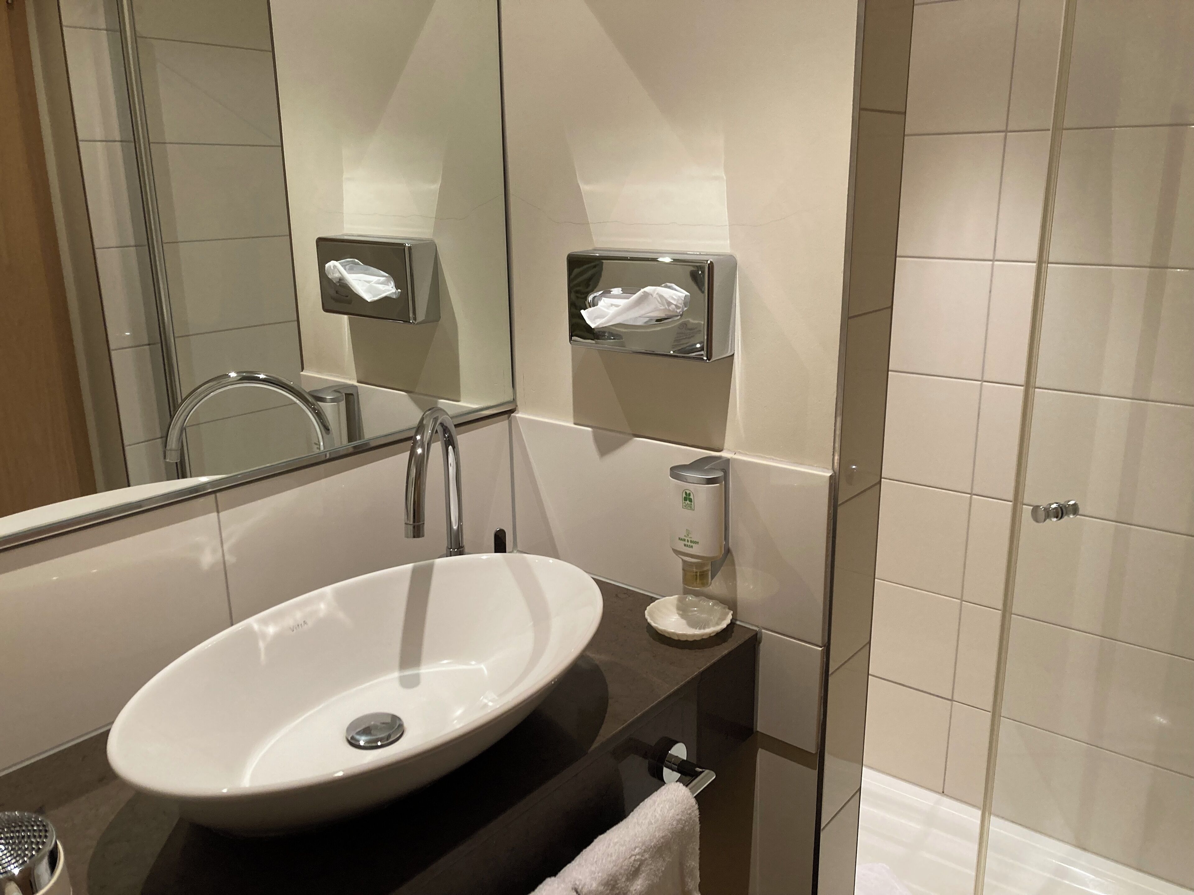 Ein modernes Badezimmer mit einem großen, ovalen Waschbecken, einem Spiegel, einem Handtuchhalter und einer Seifenspender.