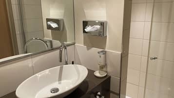 A modern bathroom with a large oval sink, a mirror, a towel rack, and a soap dispenser.