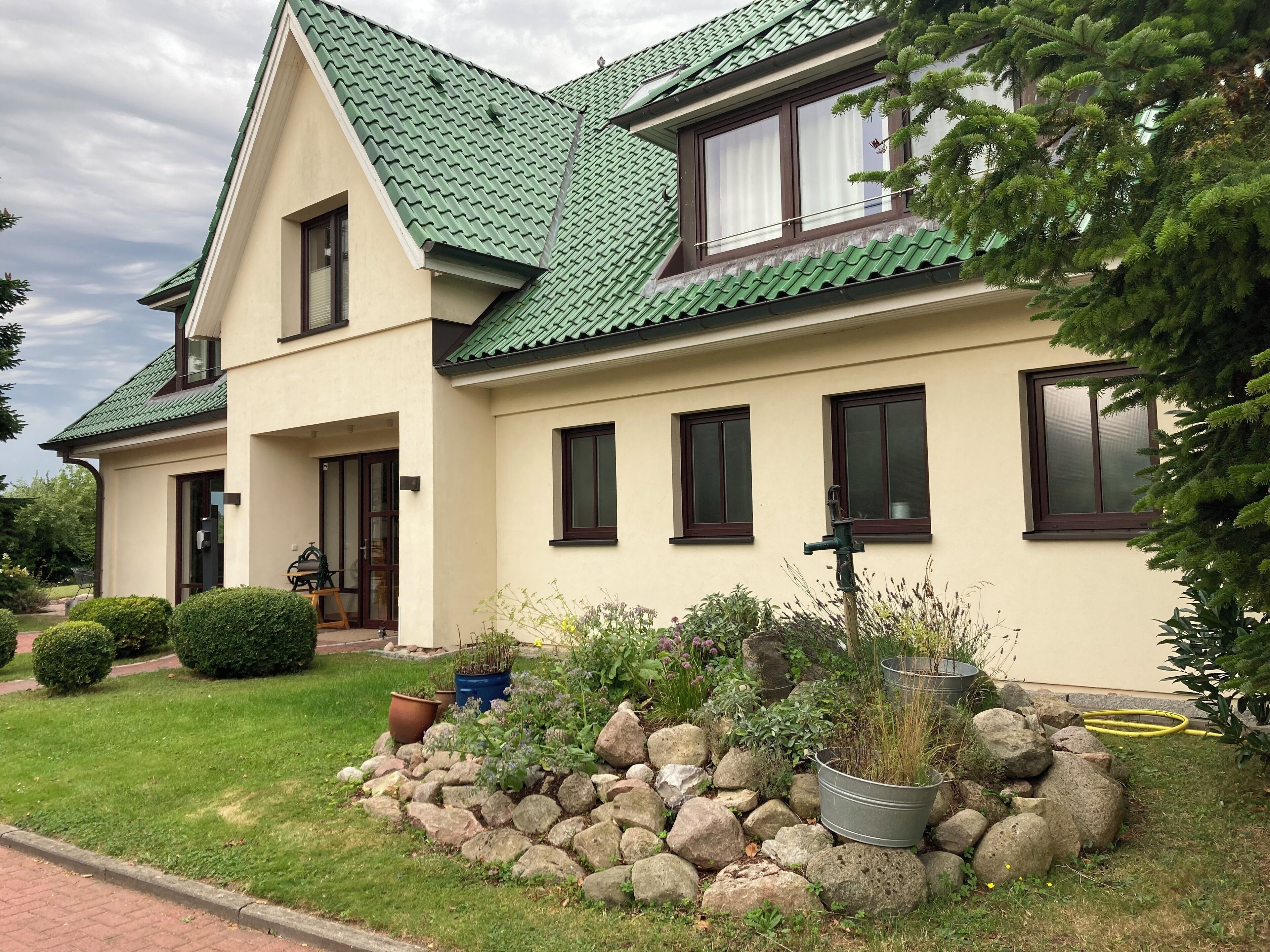 Een twee verdiepingen tellend huis met een groen dak, een voortuin en een tuin met een keienrand.