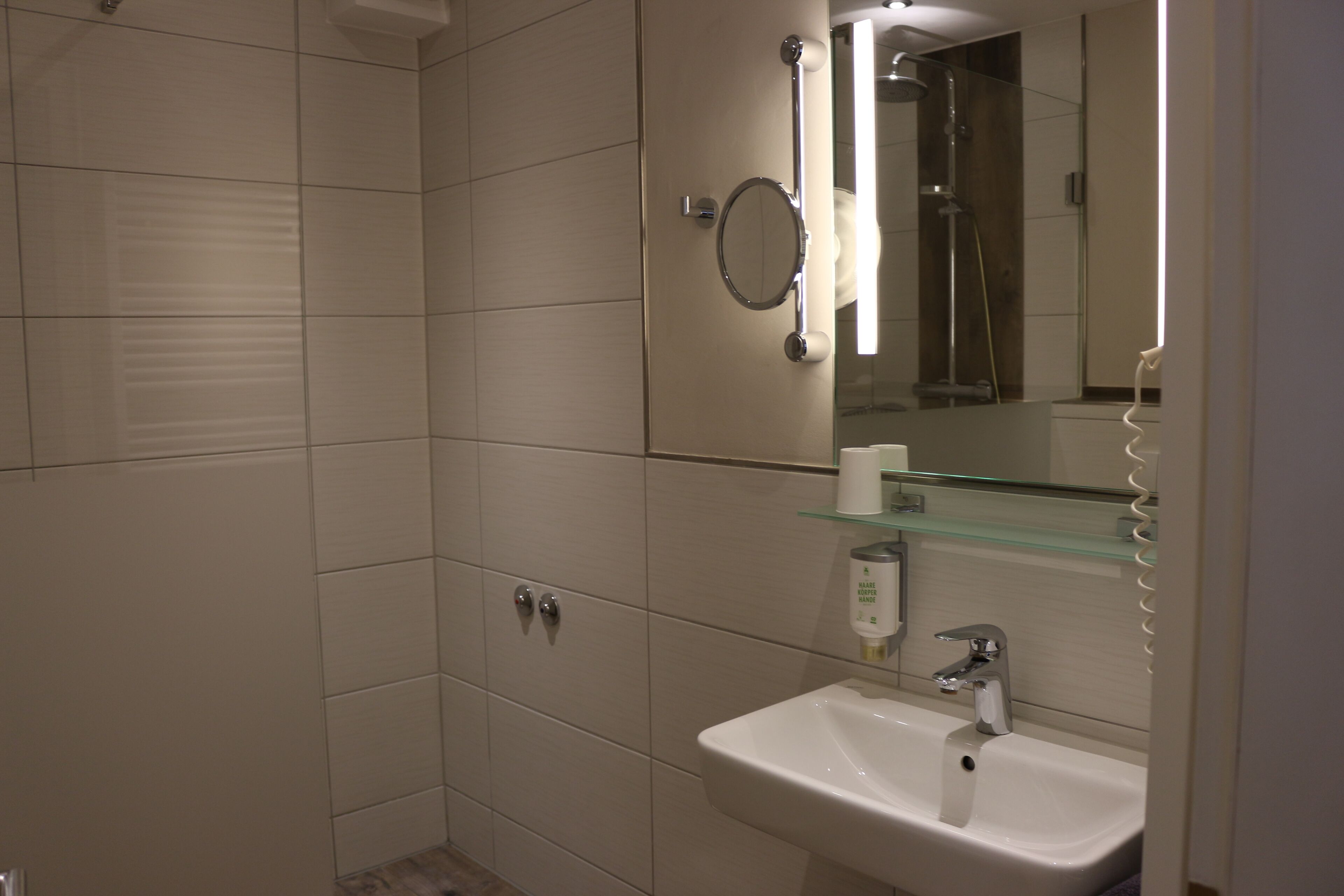 Un baño con un lavamanos blanco, un espejo y una repisa de vidrio.