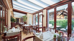 A restaurant with wooden tables and chairs, a tiled floor, and large windows offering a view of the outdoors.