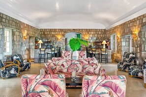 A spacious lounge with a stone wall backdrop, a bar area with a variety of bottles, and tropical-themed seating.